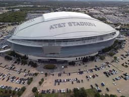 Dallas — AT&T Stadium: aerial view of a large silver domed stadium surrounded by parking lots.