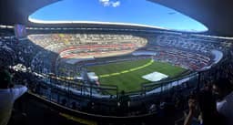 Mexico City — Estadio Azteca: aerial view of a large open stadium with a green field under a clear sky.