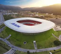 Guadalajara — Estadio Akron: aerial view of a stadium with a white ring-shaped roof set in green hills.