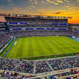 Philadelphia — Lincoln Financial Field: open stadium at sunset with a green field and orange sky behind it.