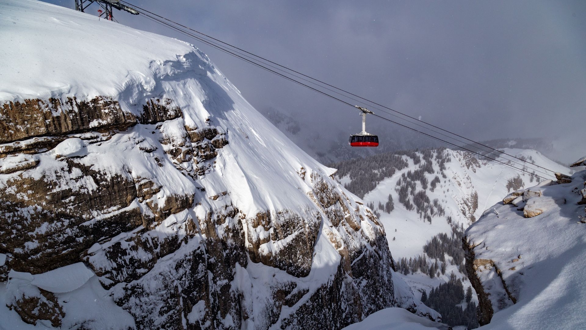 The Jackson Hole Aerial Tram, known as Big Red, traveling above snowy cliffs and forested slopes on Rendezvous Mountain