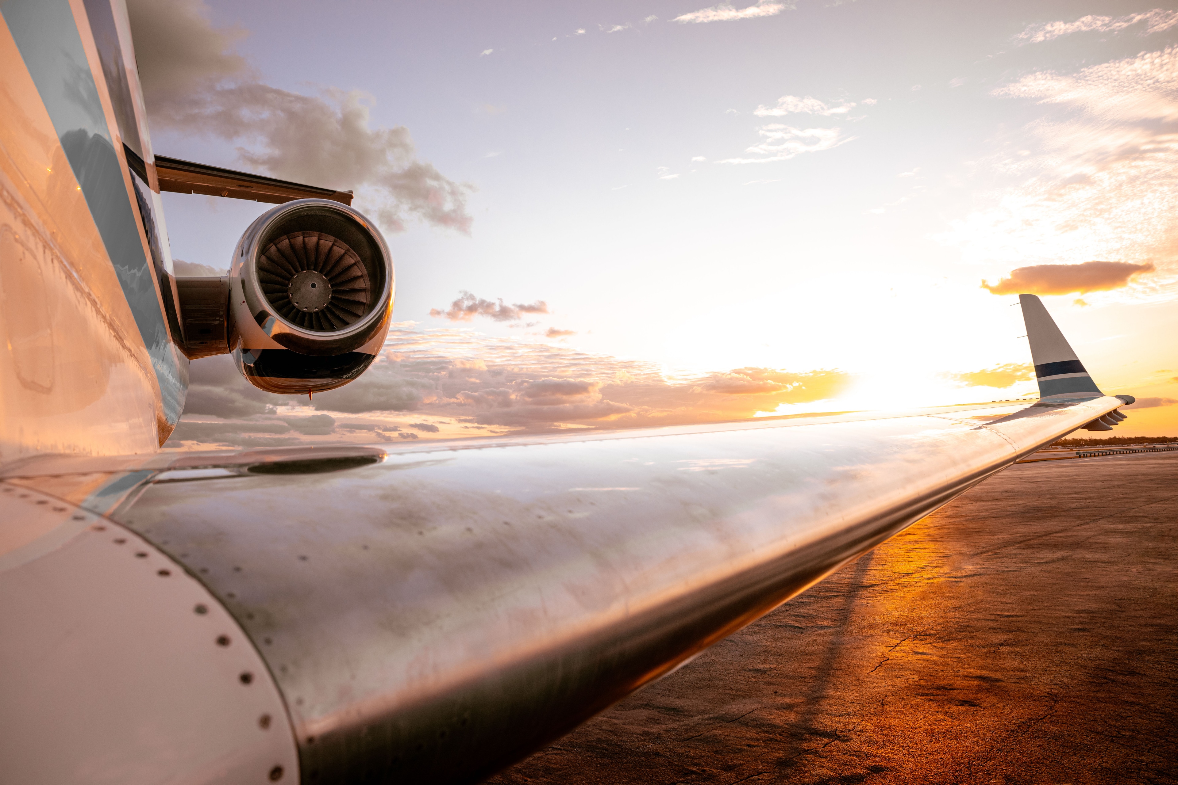 Close-up of a private jet engine and wing at sunset, reflecting golden light on the tarmac.