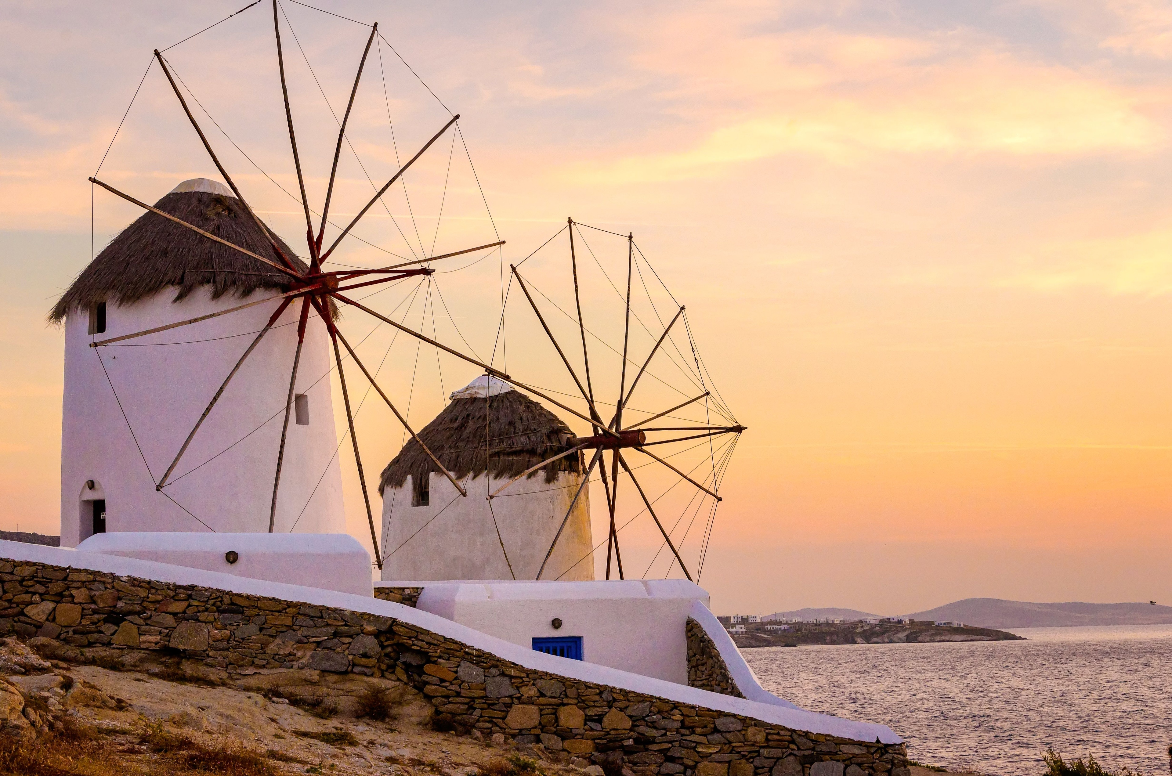 Traditional white windmills on the coast of Mykonos at sunset, overlooking the Aegean Sea.