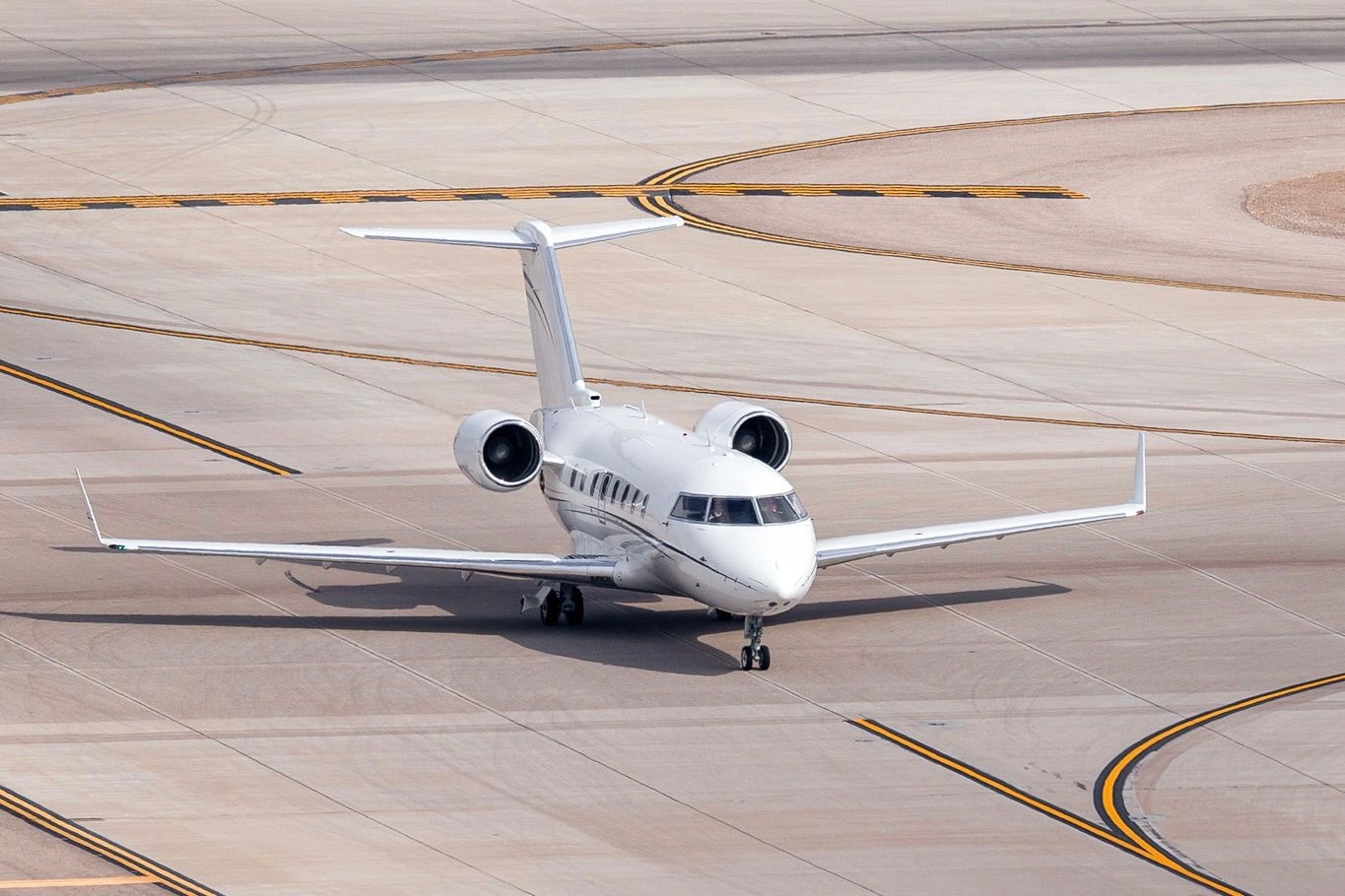 A sleek white private jet taxiing on the runway, captured from above as it prepares for departure, showcasing the streamlined design and power of modern private aviation. 
