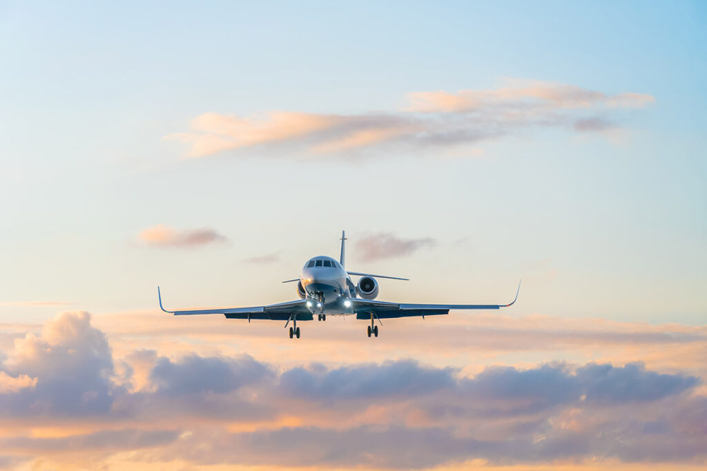 A private jet approaches landing against a backdrop of a sunset-streaked sky.